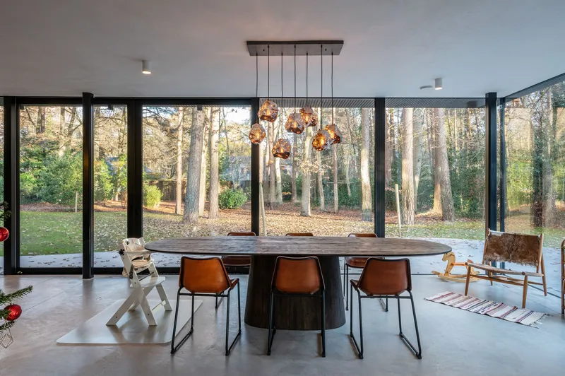 Dining area with full-height glazing overlooking woodland in late afternoon light