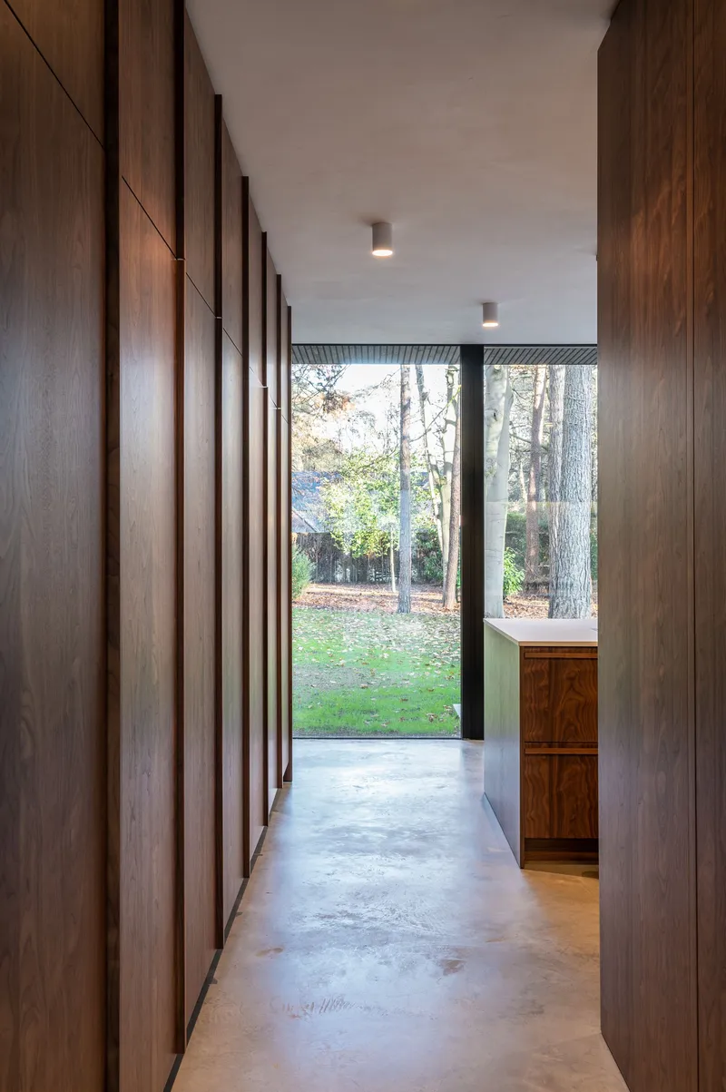 Corridor with vertical timber slatted wall leading to glazed opening framed by trees