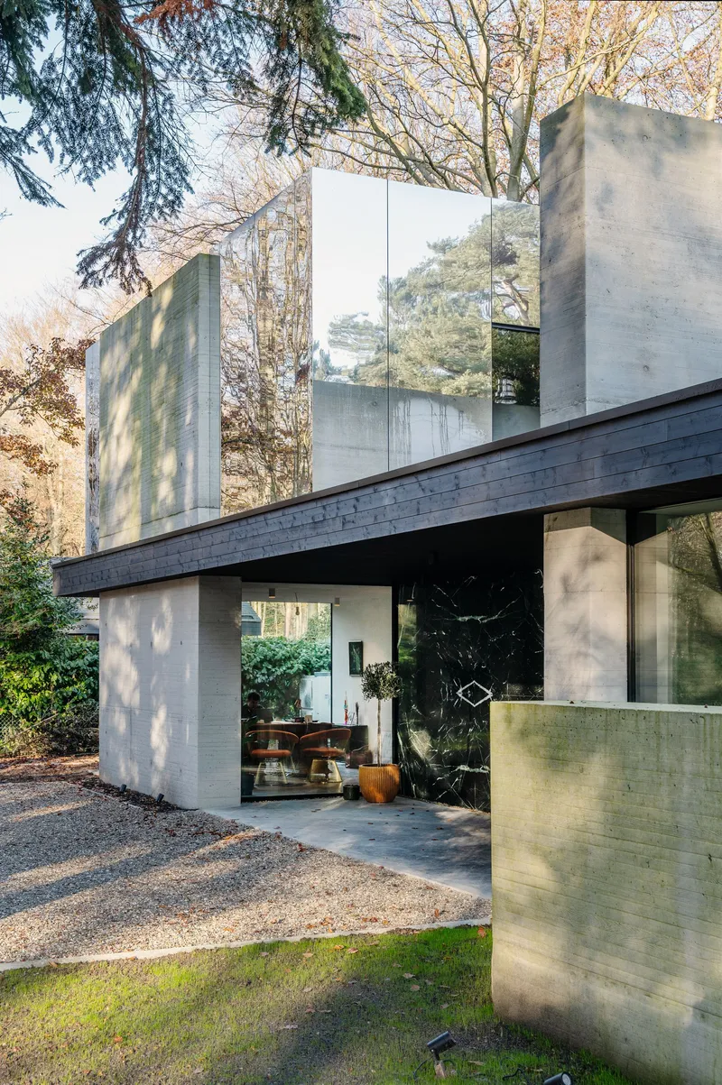 Concrete entrance canopy with exposed aggregate ground plane and dappled tree shadows across the facade