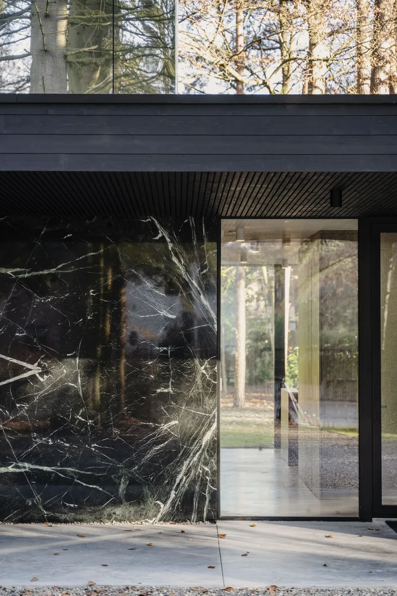 Black marble veneer facade with sliding glass door framed by autumn trees and gravel patio