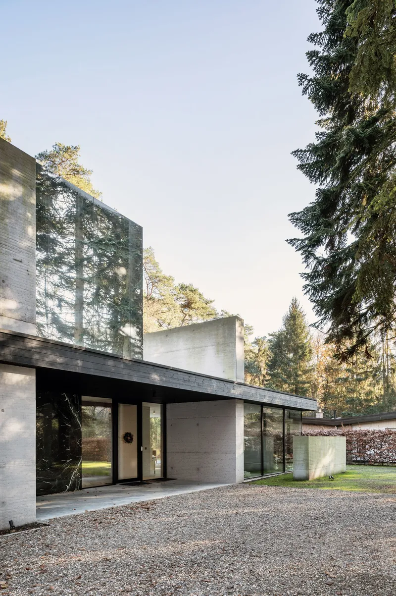 Entrance facade combining concrete walls and dark stone panels beneath a cantilevered black soffit