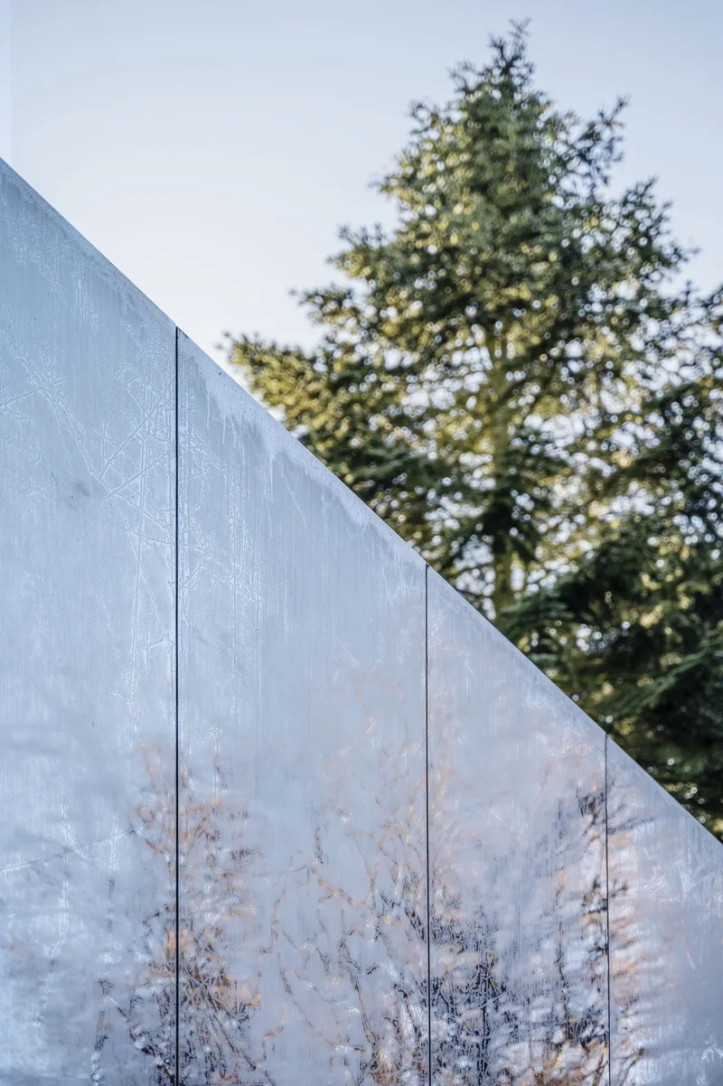 Angled concrete wall panel with tree shadows cast across its surface at dusk