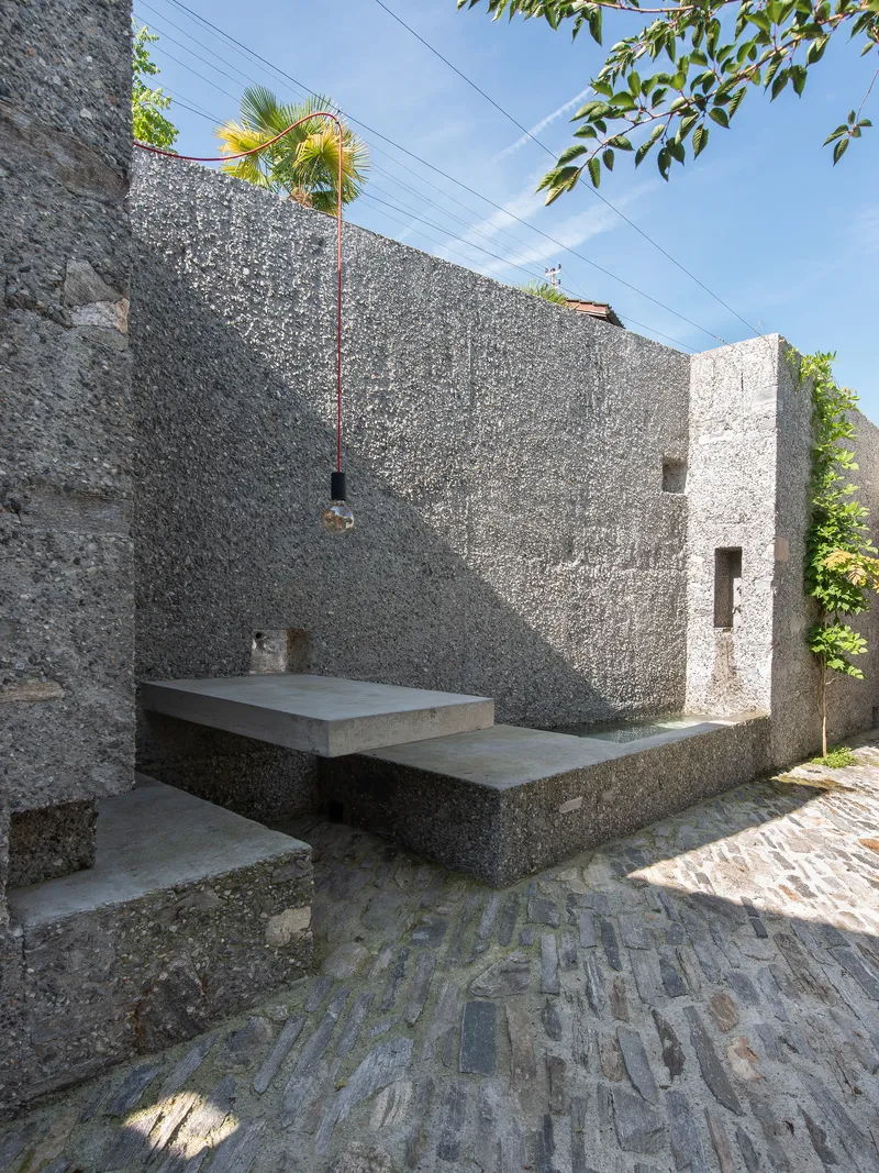 Outdoor courtyard with cantilevered concrete bench, exposed aggregate walls, and pendant light under palm fronds