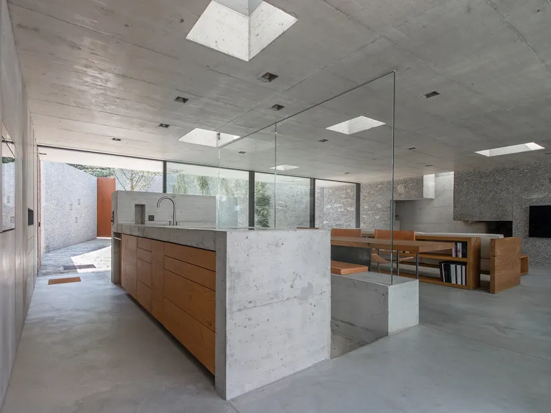 Kitchen island with timber cabinetry and concrete waterfall edge opening to courtyard through floor-to-ceiling glazing