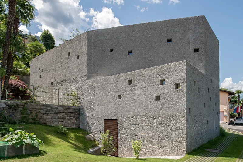 Two-tone aggregate concrete facade with scattered square openings and timber door at ground level