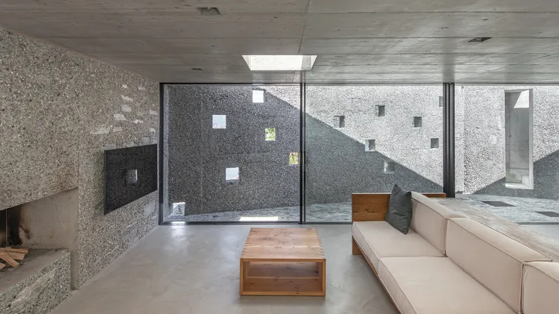 Living room with concrete ceiling and floor-to-ceiling glazing framing an interior courtyard with exposed concrete walls