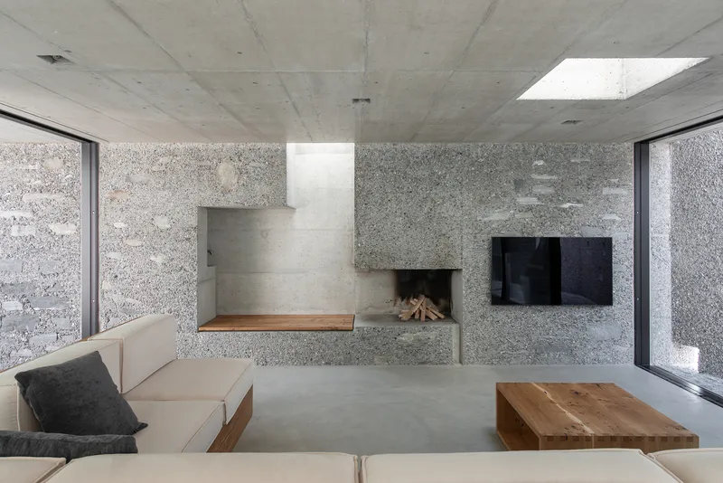 Fireplace and seating niche in aggregate concrete wall beneath skylight with exposed concrete ceiling
