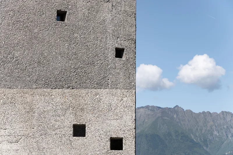 Textured aggregate concrete wall with punched square openings against distant mountain range and blue sky
