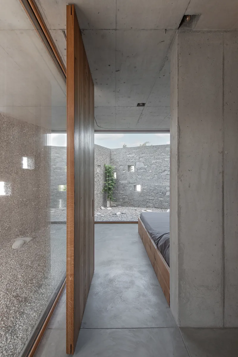 Narrow hallway with timber panel walls and polished concrete floor leading to a pebbled courtyard