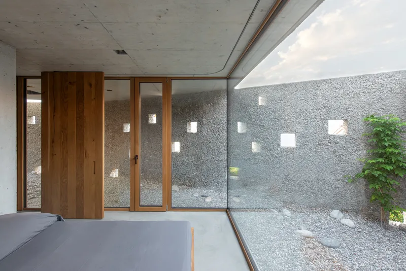 Pivoting timber door panels opening onto a gravel courtyard with punched window openings
