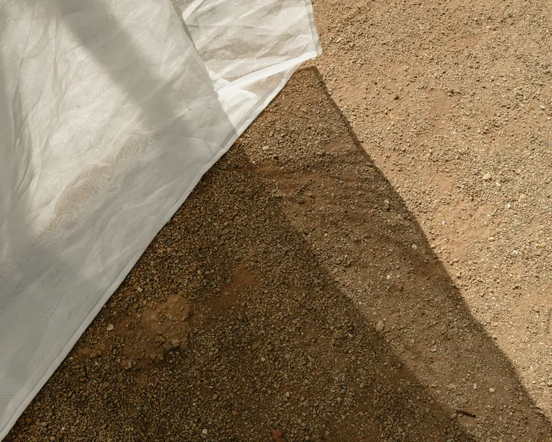 White fabric draped over a triangular formwork casts shadows onto the textured sand surface below