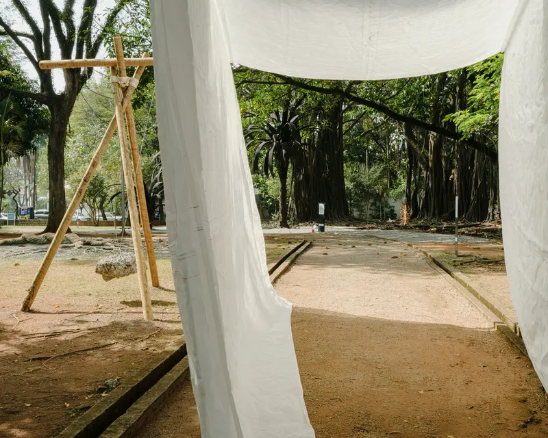 Timber tripod structure and white fabric canopy framing a grove of mature trees beyond the sand platform