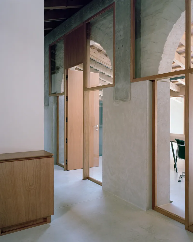 Interior hallway with timber-framed glass partitions and exposed green steel beams beneath a painted plaster vault