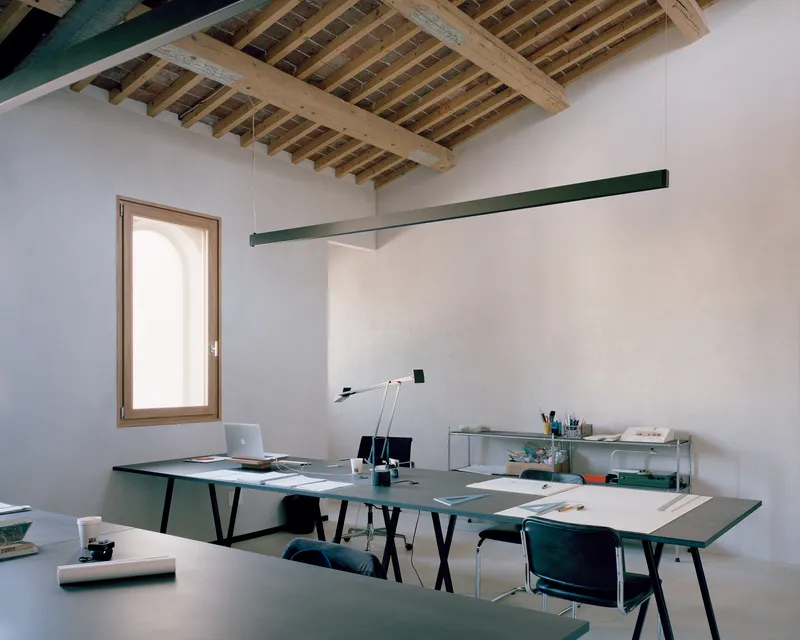 Office workspace with exposed timber ceiling joists and green desk surfaces under natural daylight from arched window