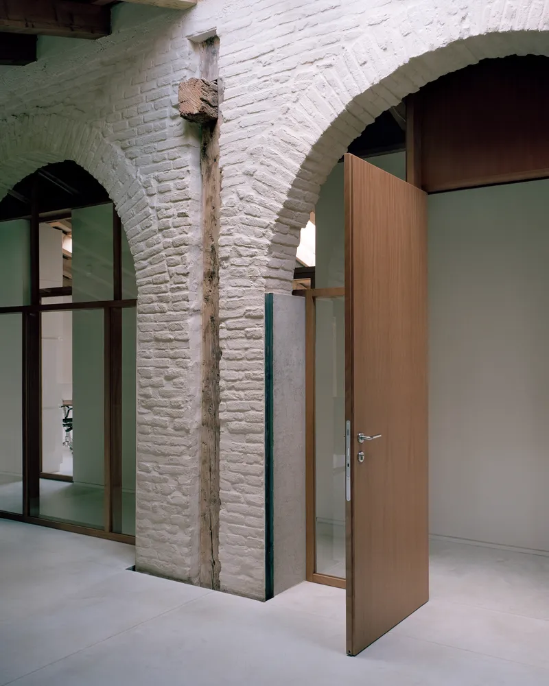 Whitewashed brick arches flanking timber door and glazed partition with visible timber column remnant between openings
