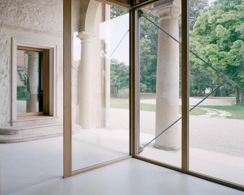 Open glass door framing a view of stone columns and a gravel courtyard with trees beyond