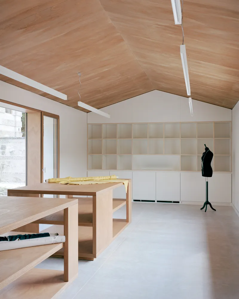 Workspace with pitched timber ceiling, built-in shelving, and timber work tables on pale floor