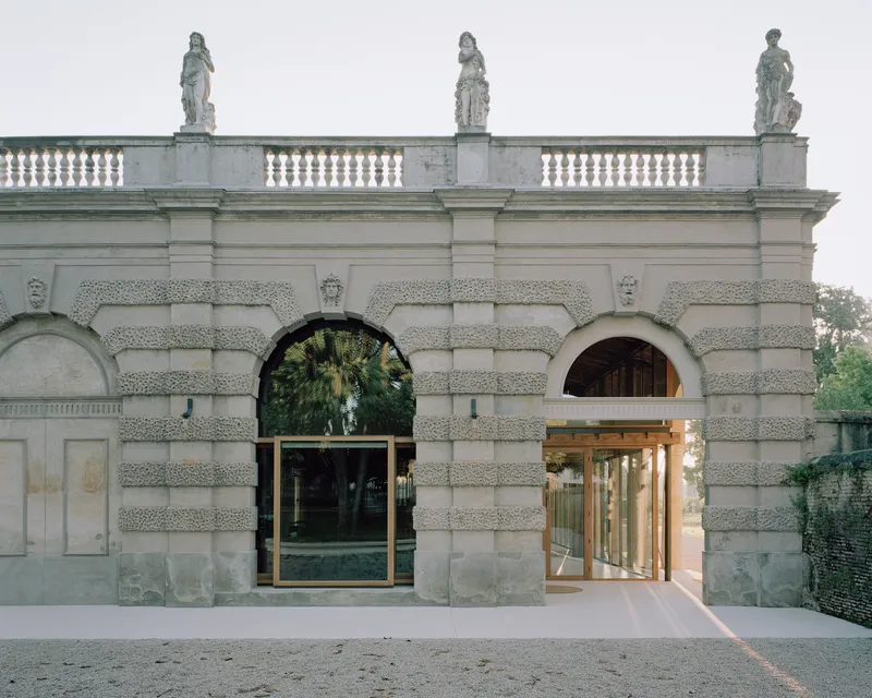 Rusticated stone gateway with arched openings flanked by new bronze-framed glass doors at dusk