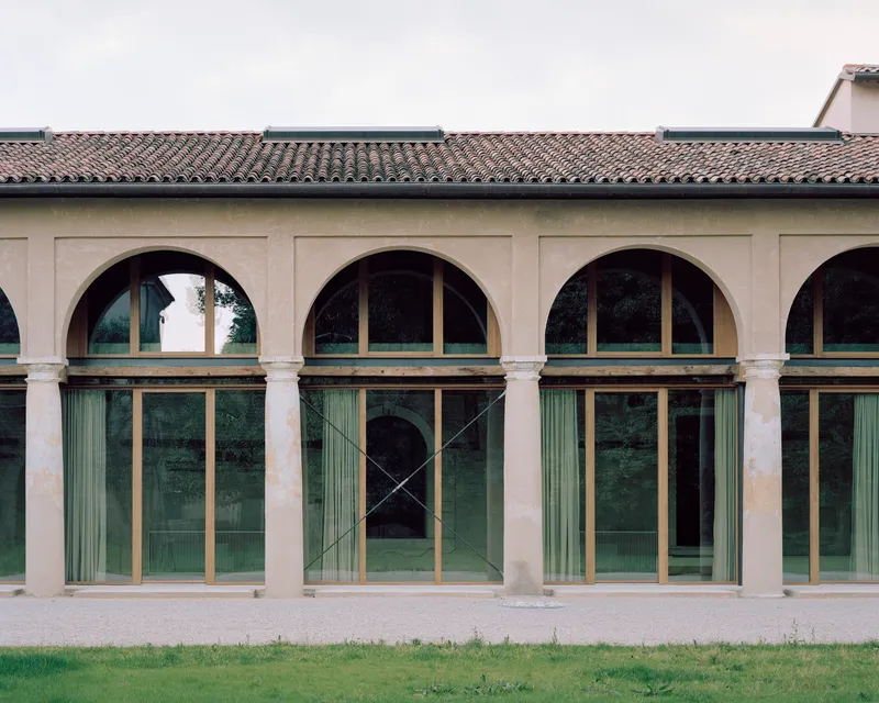 Arcade facade with arched openings and glazed bronze-framed doors beneath a tiled roof