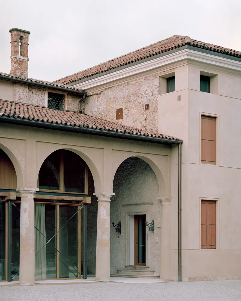 Courtyard view showing the arcade, arched entry portal, and historic brick chimney under overcast sky