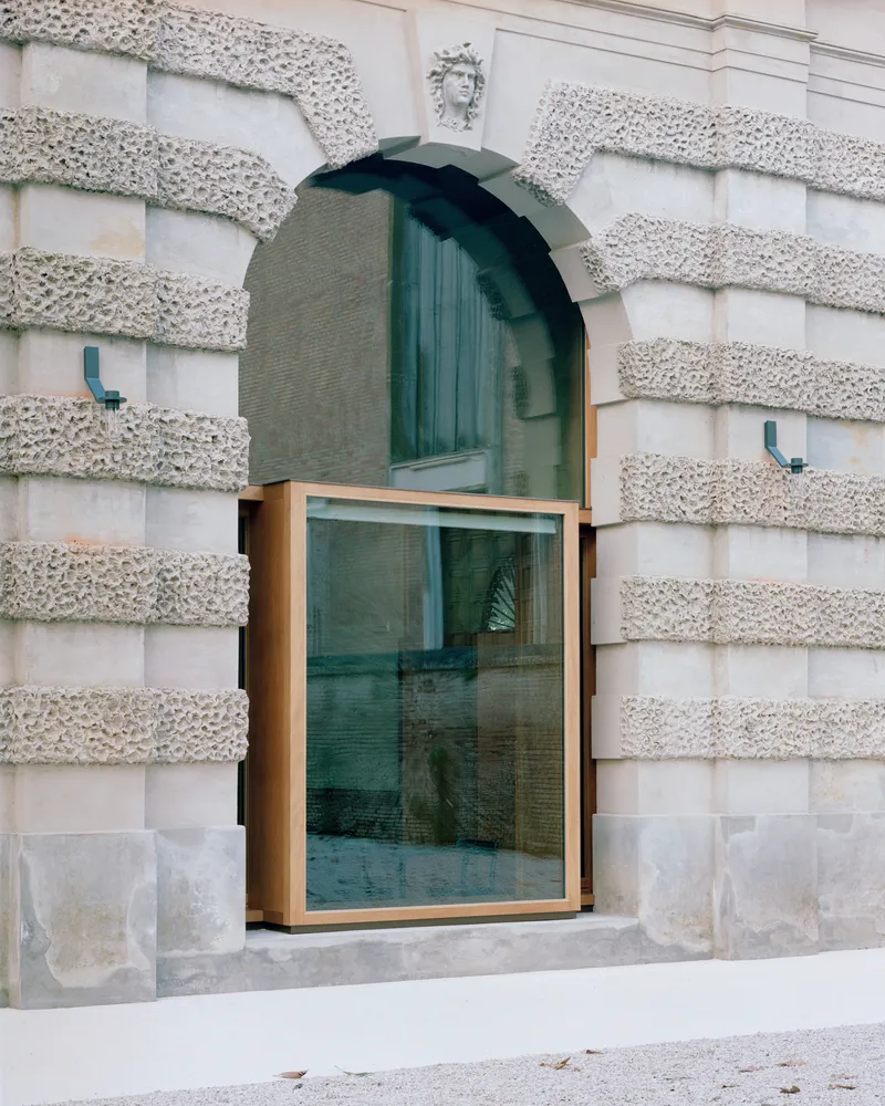 Bronze-framed glass window inserted into a rusticated stone facade with arched opening above