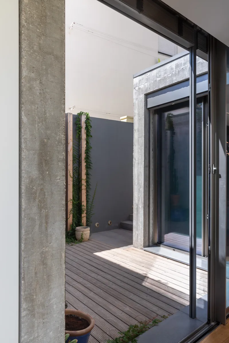 View through sliding glass doors to courtyard with exposed concrete column and timber deck under bright daylight