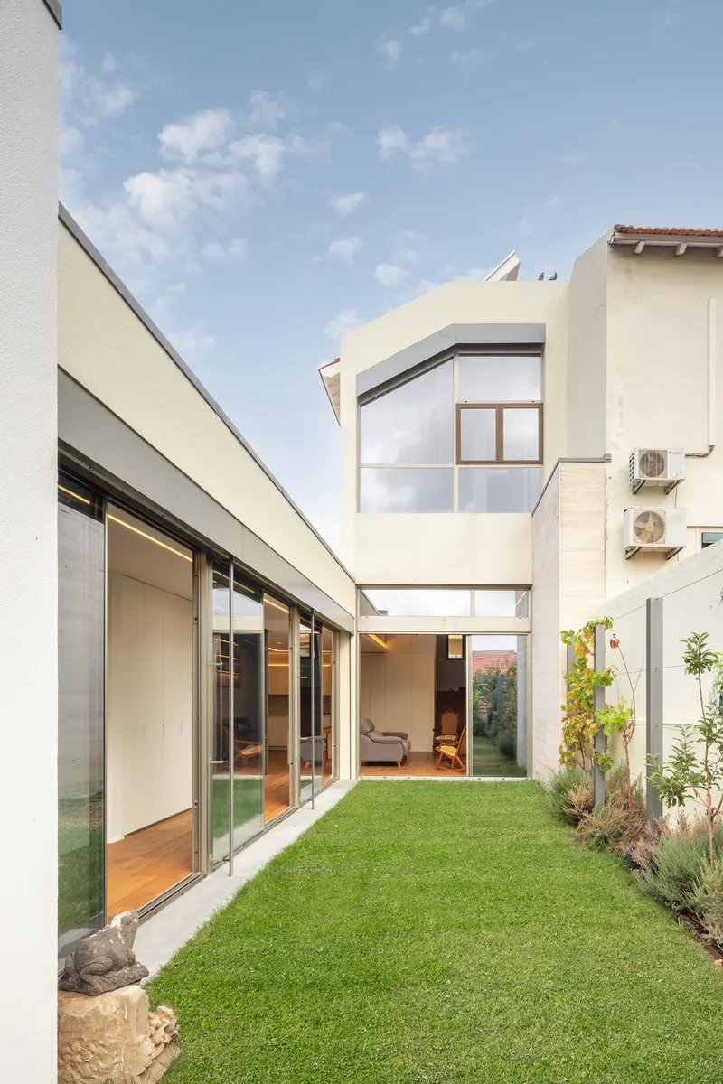 Courtyard with lawn connecting two white volumes with full-height glazing under a blue sky