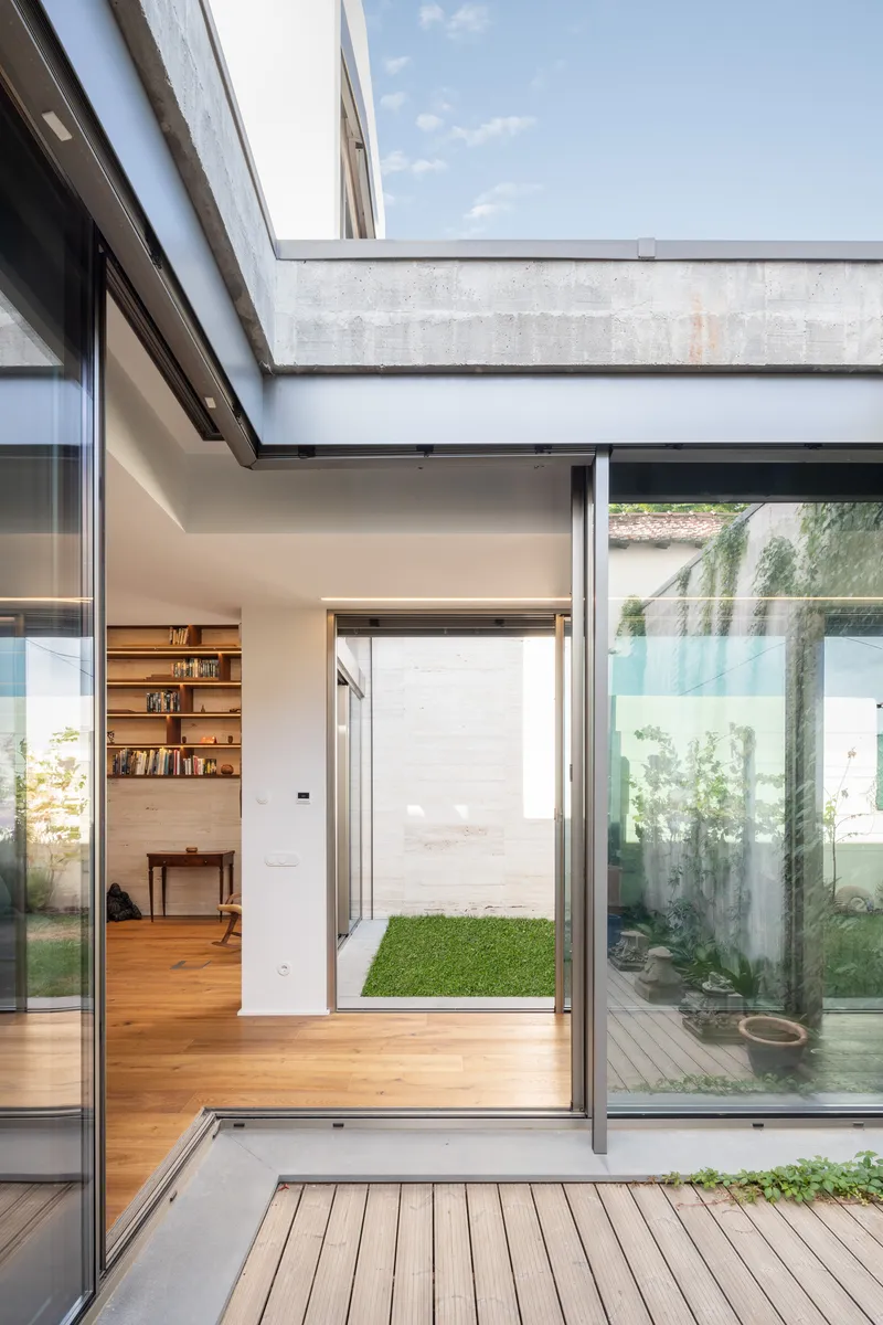 Concrete beam spanning above timber deck and glass doors framing views into interior spaces