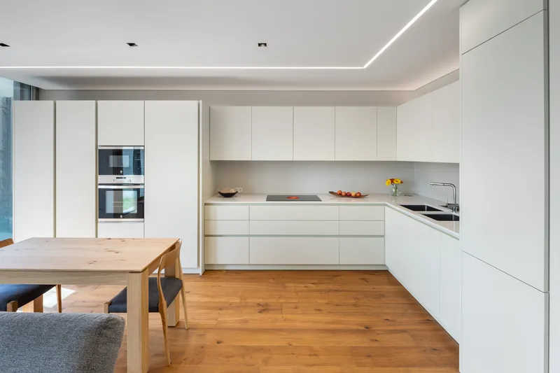 White kitchen with handleless cabinetry and continuous cove lighting above oak timber floors