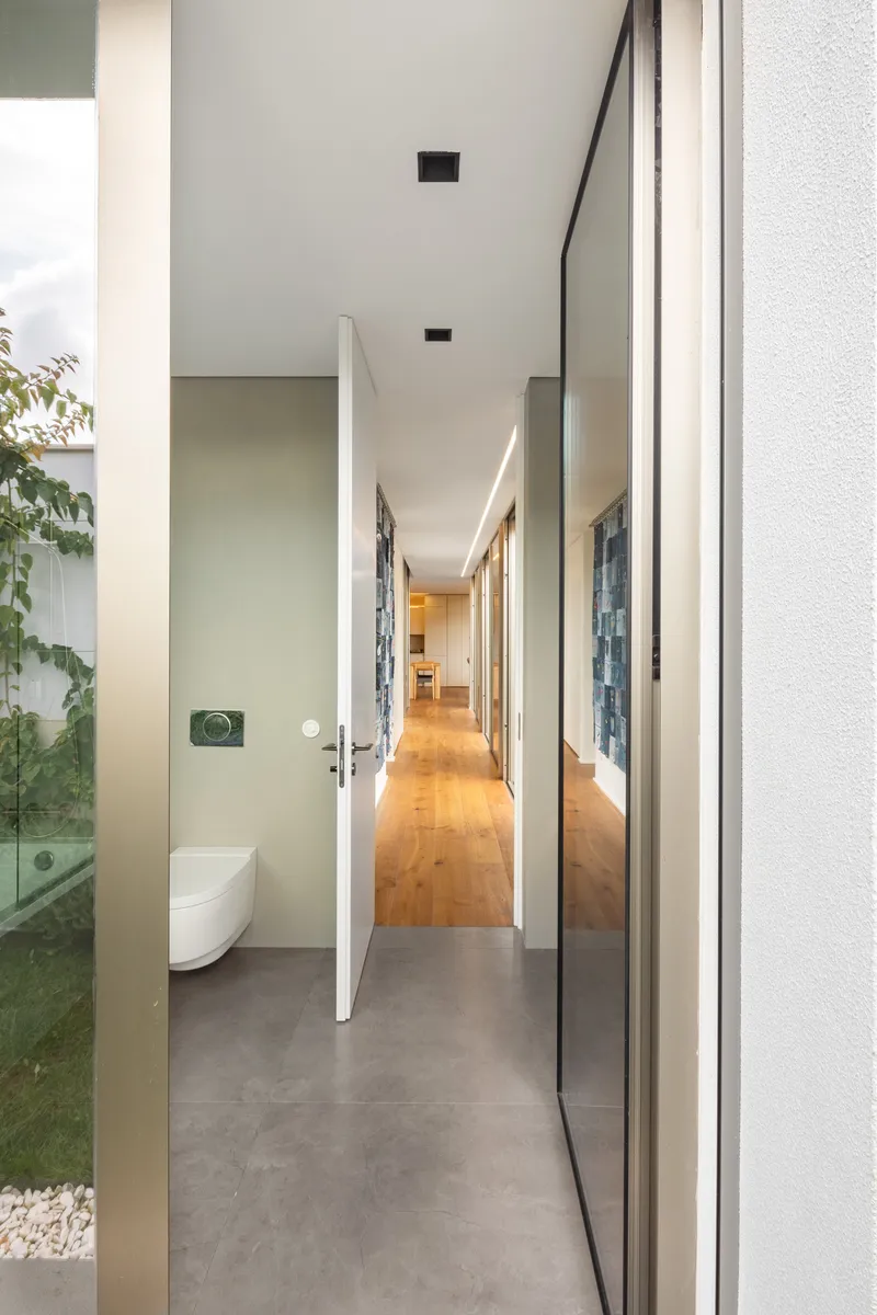 Interior hallway with polished concrete floor looking past a bathroom door toward timber flooring beyond