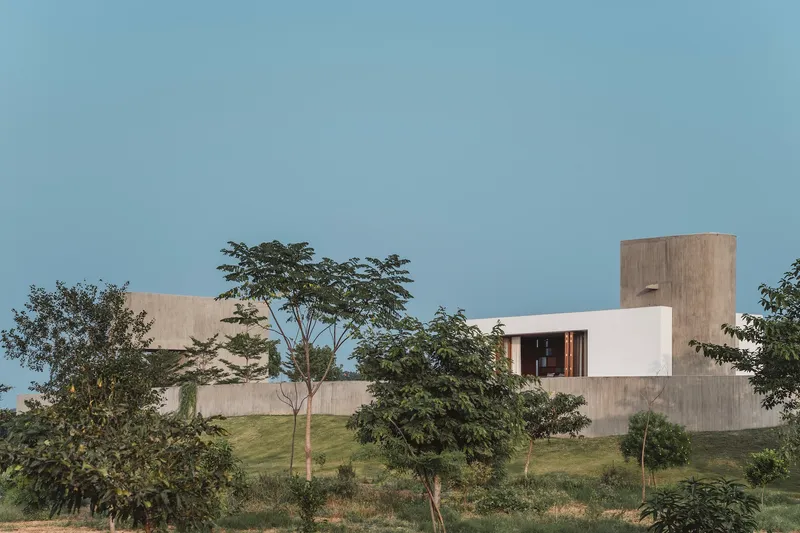 Board-formed concrete volumes and white plaster walls set among young trees on a grassy hillside