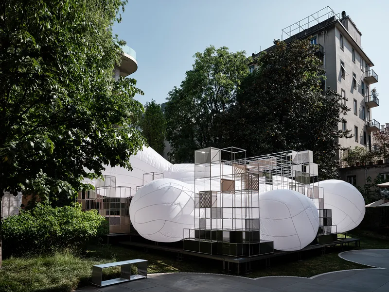 White inflated sculptural volumes anchored by a central steel grid scaffold structure in a courtyard