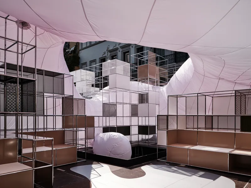 Interior view beneath the tensioned fabric canopy with modular steel shelving and white cube tower element