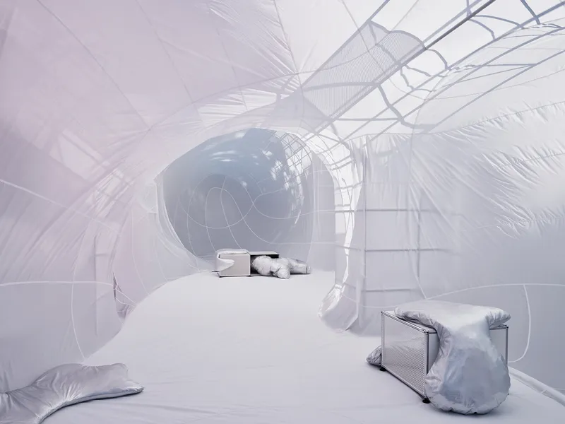 Interior of inflatable bubble with wire frame structure and scattered metallic cushions on white floor