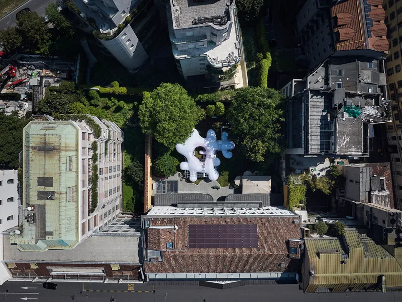 Drone view of the clustered white balloon roof set between dense urban blocks and mature tree canopy