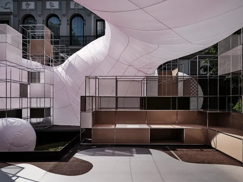 Modular bronze and glass shelving units positioned beneath the curved inflatable canopy casting shadows