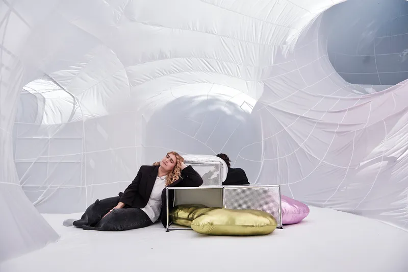 Interior view of white inflatable structures with a person reclining beside metal shelving and gold cushions