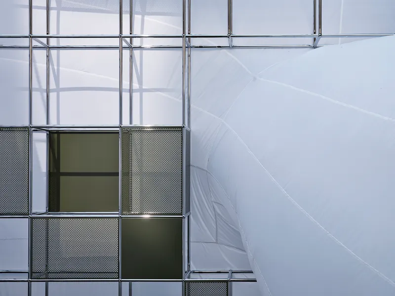 Close-up of modular metal shelving with perforated panels and tinted glass against white inflatable walls