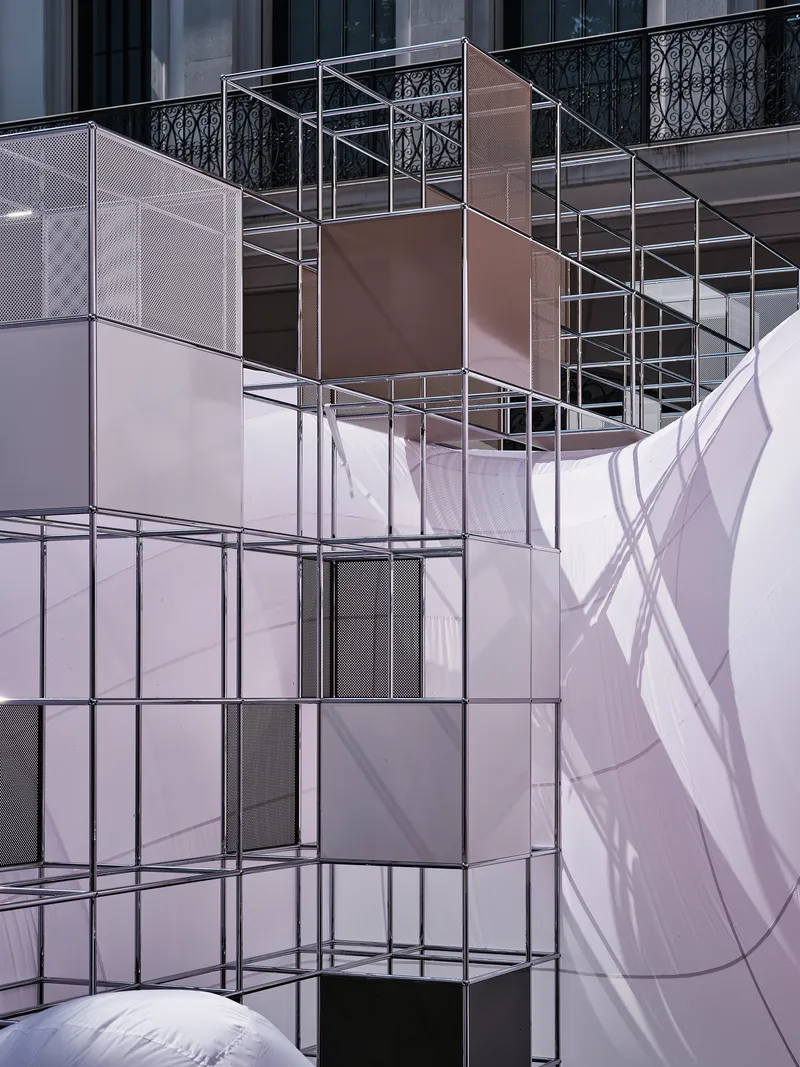 Stacked cubic shelving modules with clear and bronze panels casting shadows on white fabric surfaces