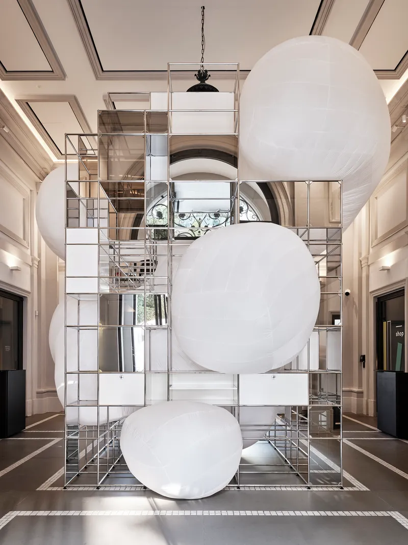 Double-height lobby with suspended white spherical balloons in front of mirrored metal grid storage tower