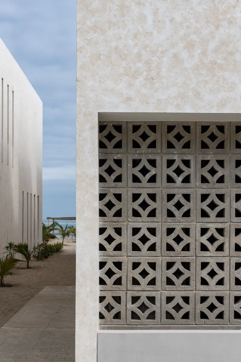 Courtyard view with geometric breeze block screen set within a pale stucco facade under soft clouds