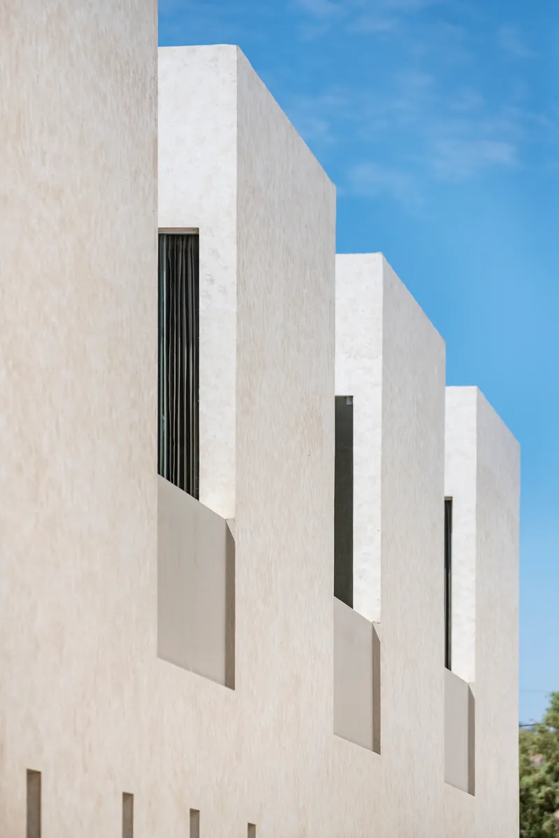 Stepped white facade with recessed vertical window openings against a clear blue sky