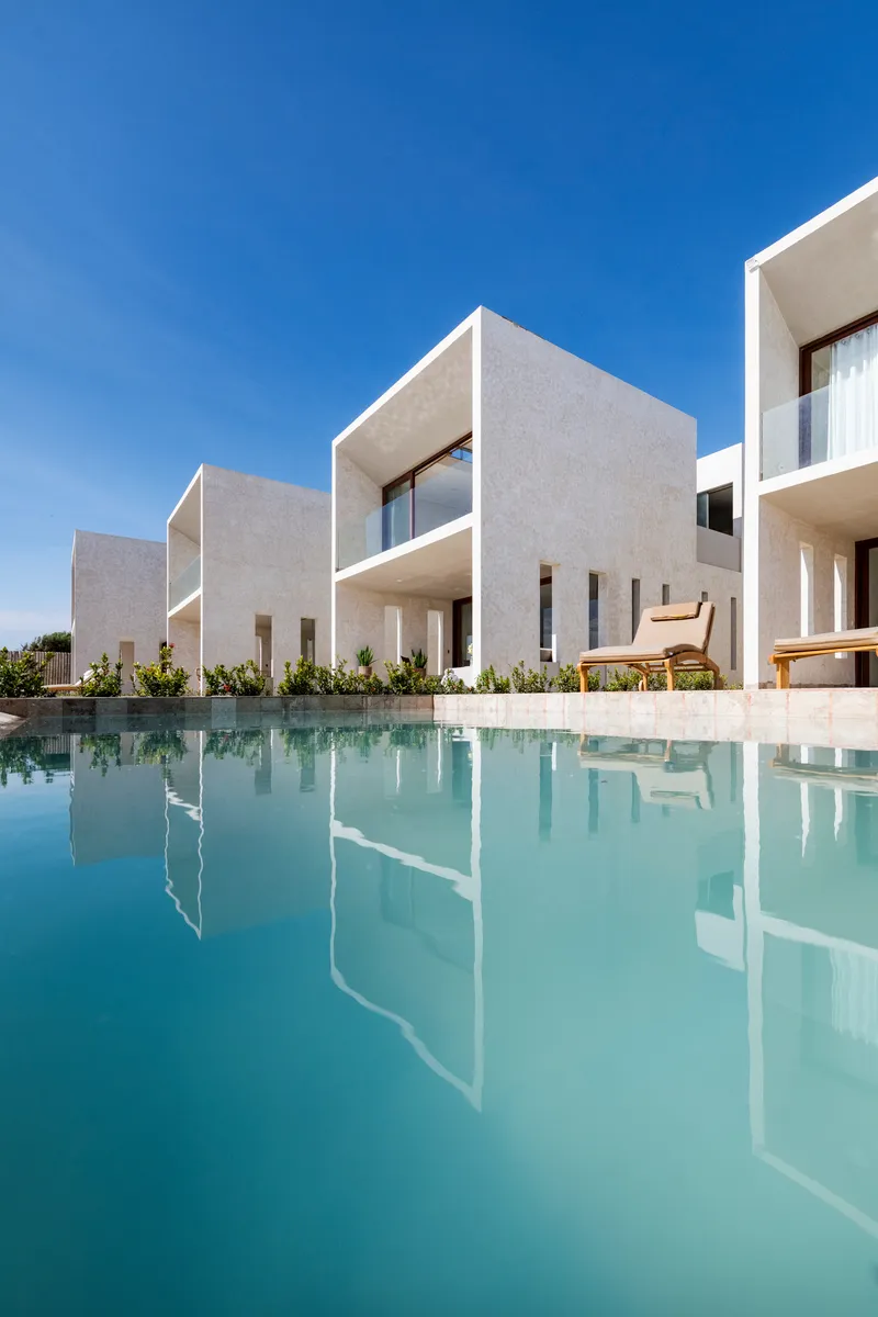White cubic volumes reflected in a still rectangular pool under clear blue sky