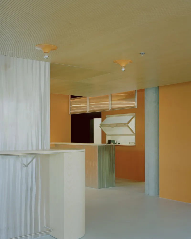 Interior view showing orange walls, timber clerestory windows, and a white curtain beside concrete columns