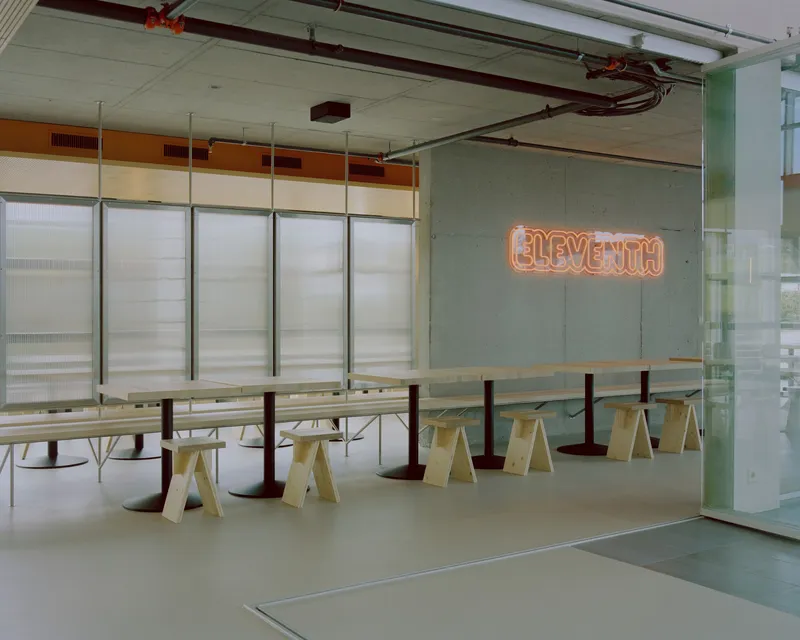 Cafeteria space with orange neon signage mounted on a concrete wall beside translucent partition panels