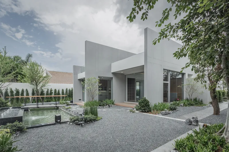White stucco facade with recessed entry and shallow reflecting pool surrounded by gravel and planted beds