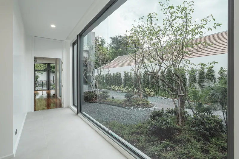 Interior corridor with polished floor opening to a gravel garden courtyard planted with slender trees