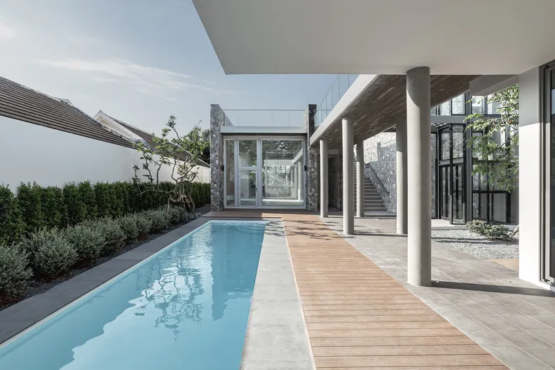 Covered terrace with white columns alongside a lap pool and timber deck opening to planted beds