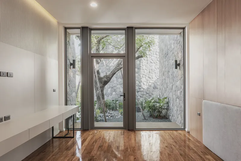 Interior bedroom with timber-lined walls and glass doors opening to courtyard with tree and stone walls