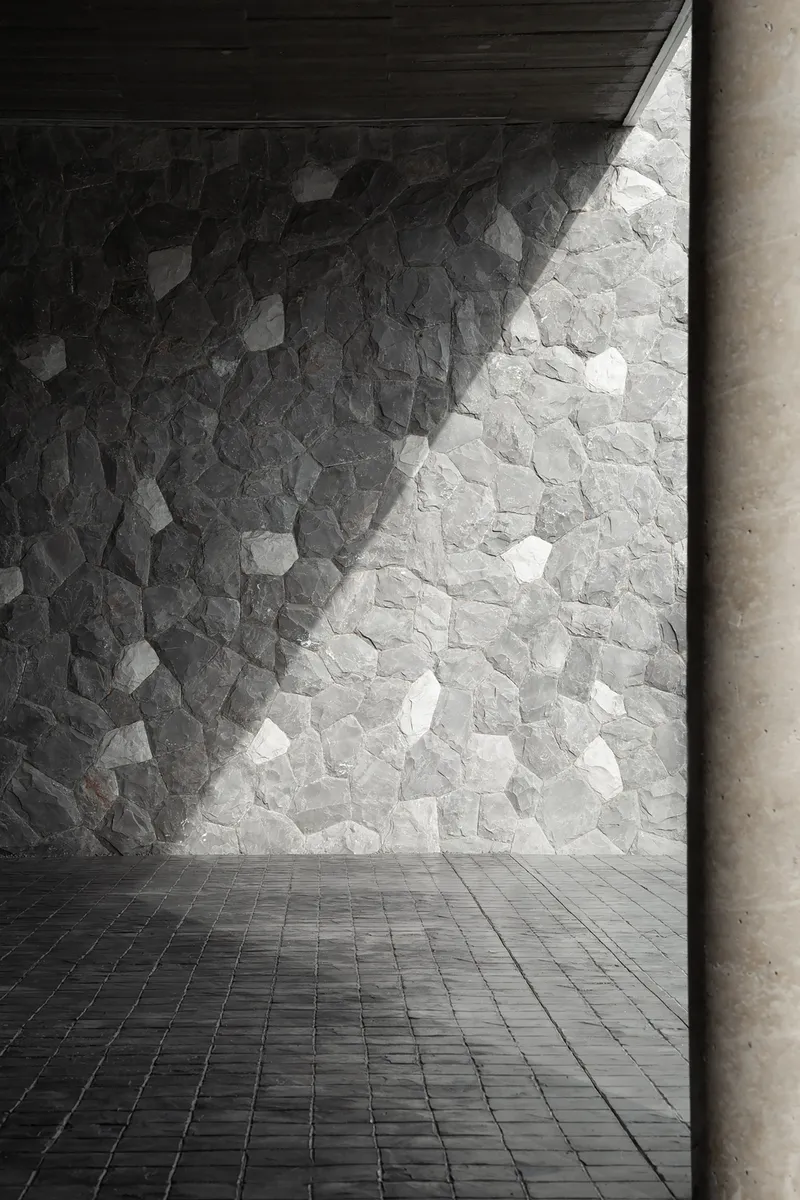 Stone-clad wall with irregular pieces in light and shadow next to a concrete column